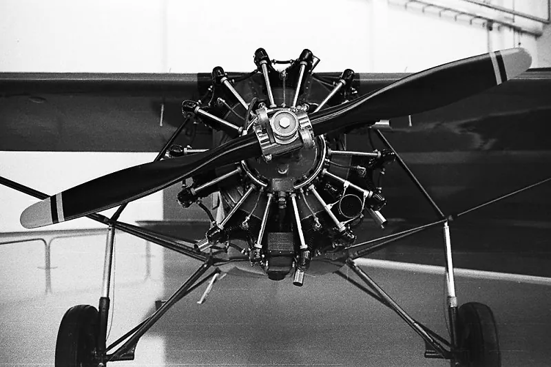 Avião antigo de hélice e motor radial visto de frente, em um hangar