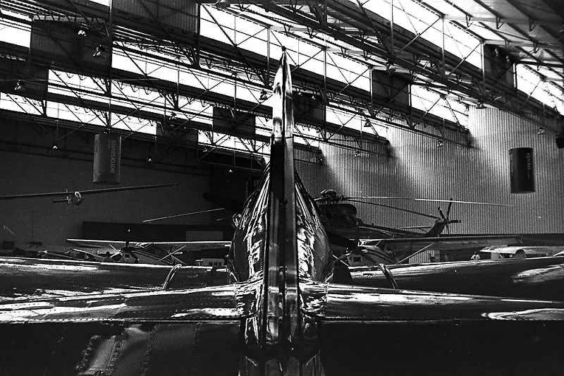 Interior de um hangar com aviões antigos, visto de baixo, sob a estrutura metálica do teto